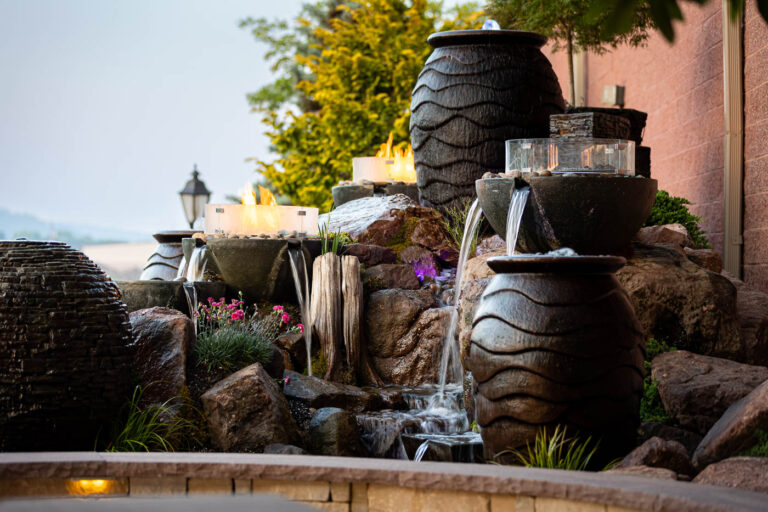 Pondless water feature with stacked stone pots, flowing water, and surrounding greenery, enhancing outdoor space aesthetics for landscaping and hardscaping solutions in Denver, PA.