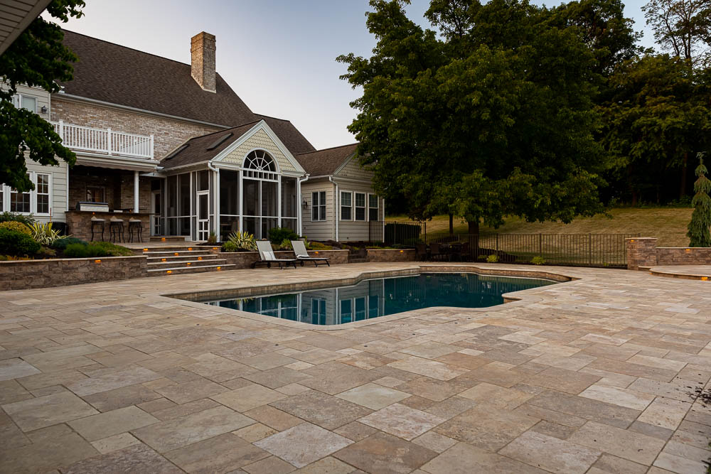 paver patio with a retaining wall with lights around a pool