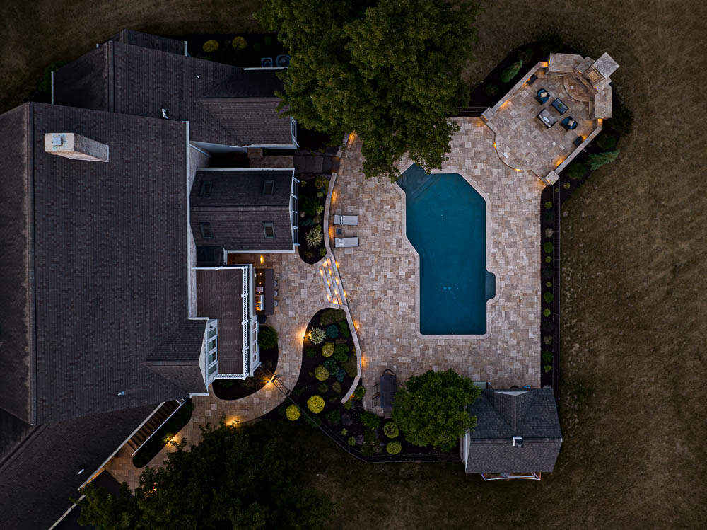 arial view of the paver patio around a pool with an outdoor fireplace