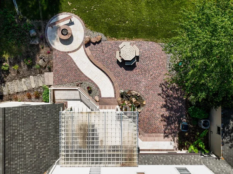 Elegant home exterior at night featuring well-lit entryway, landscaped gardens, and inviting pathway, showcasing outdoor lighting and hardscape design by Authentic Homescapes.