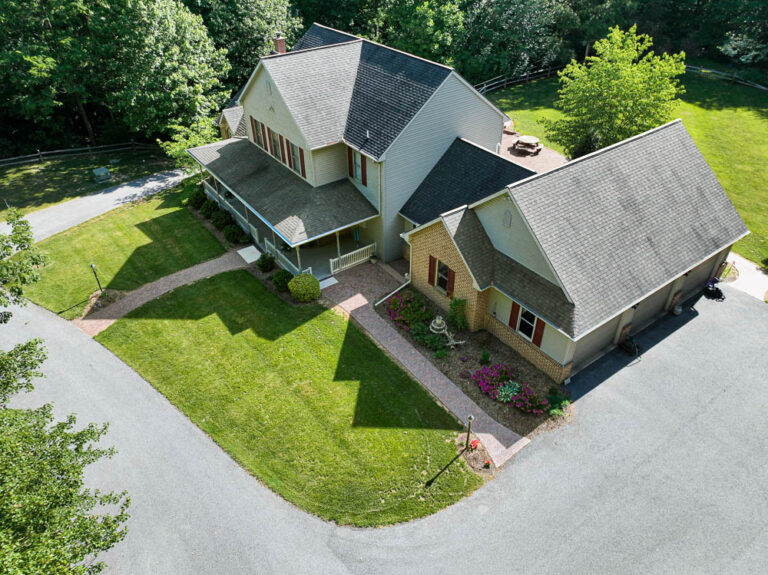 Aerial view of a well-maintained home featuring a landscaped yard with green grass, flower beds, and a winding paver walkway, emphasizing outdoor living spaces and hardscaping elements.
