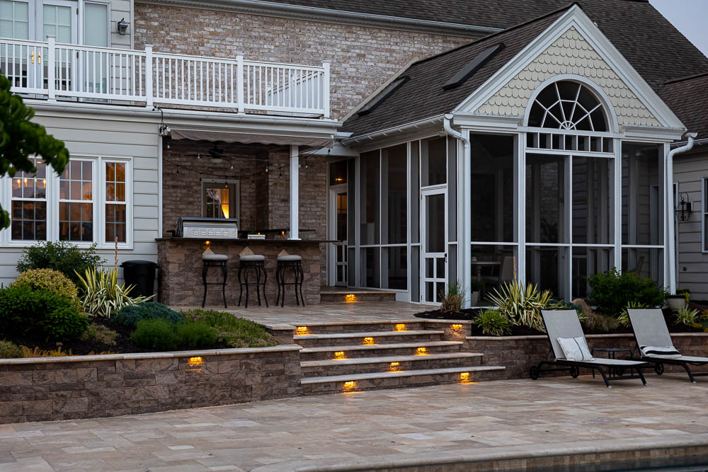 paver patio with a retaining wall with lights and outdoor kitchen