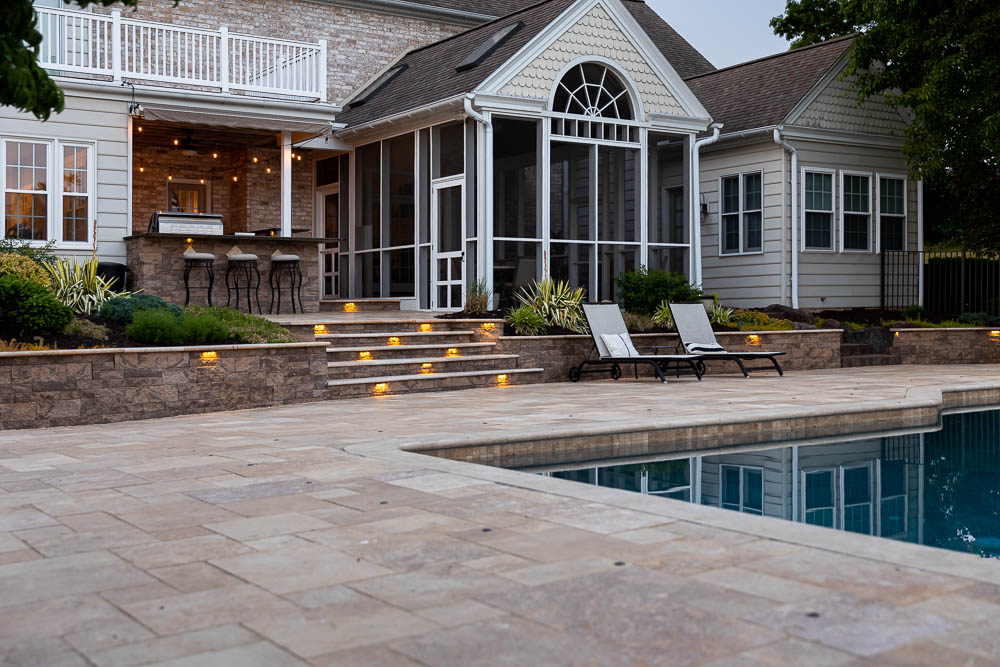 paver patio with a retaining wall with lights around a pool
